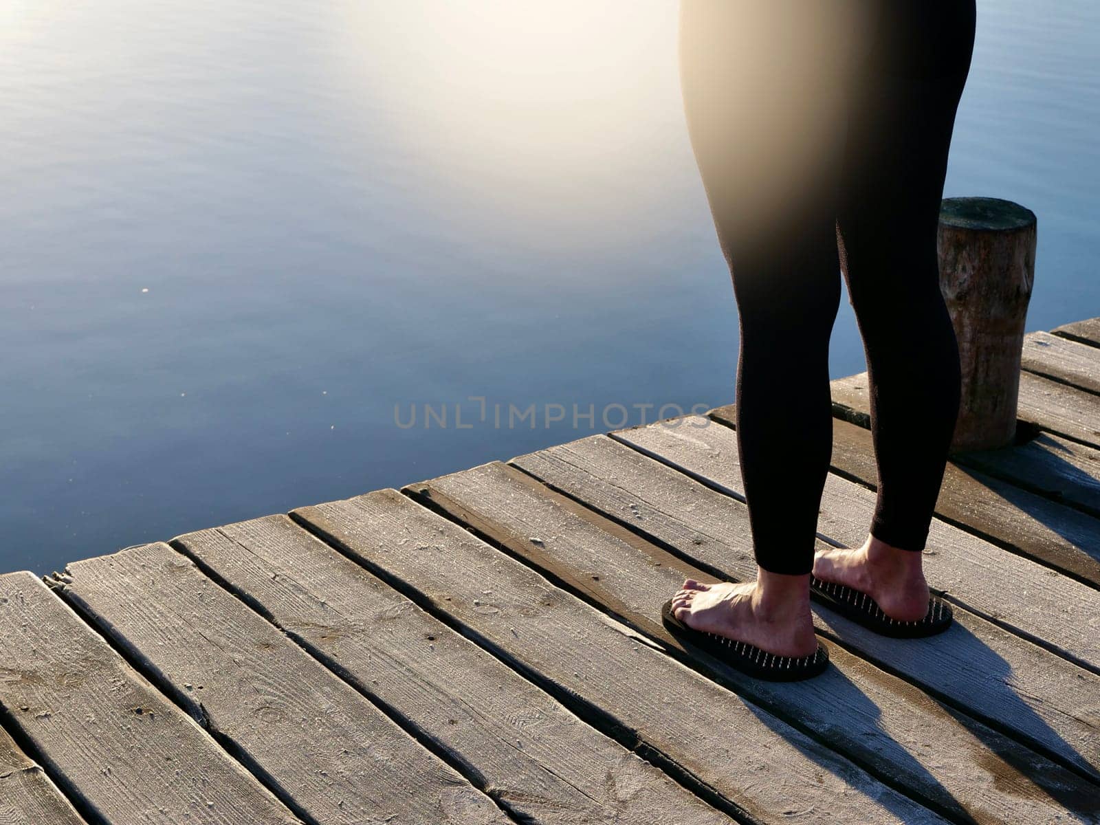 Woman standing on sadhu board, process of standing barefoot on nails, view of feet practicing yoga and meditation outdoors, autumn day near lake at sunrise