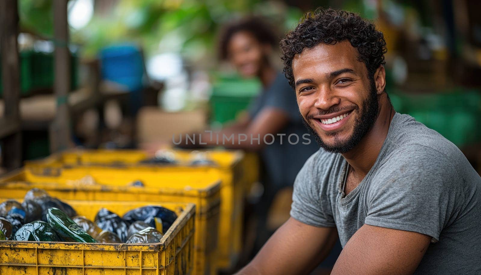 A young adult man smiles while volunteering at community recycling center, surrounded by colorful bins filled with recyclable materials