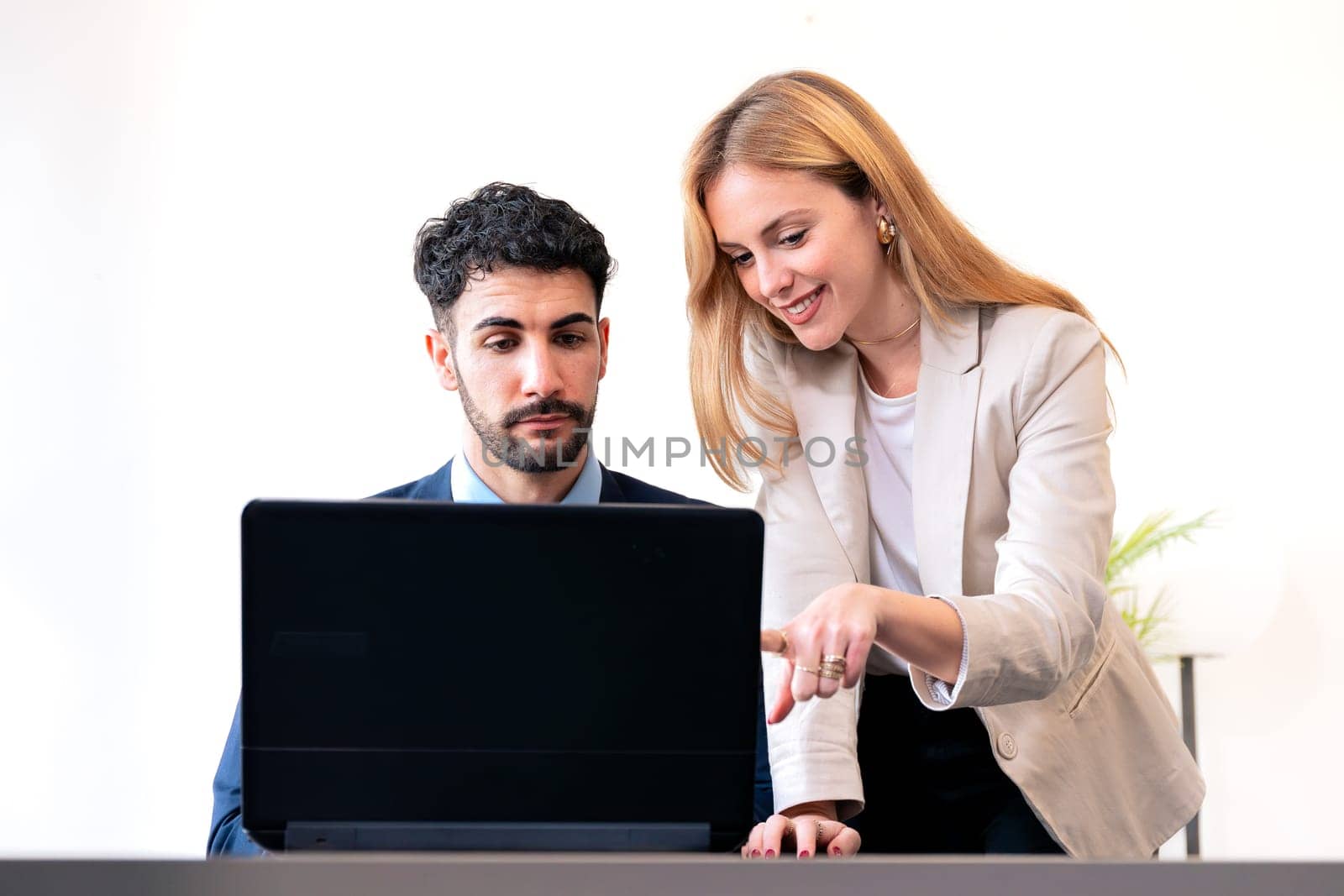 Professional man and woman working together on a laptop in a modern office. The woman points at the screen, explaining details while the man listens attentively.