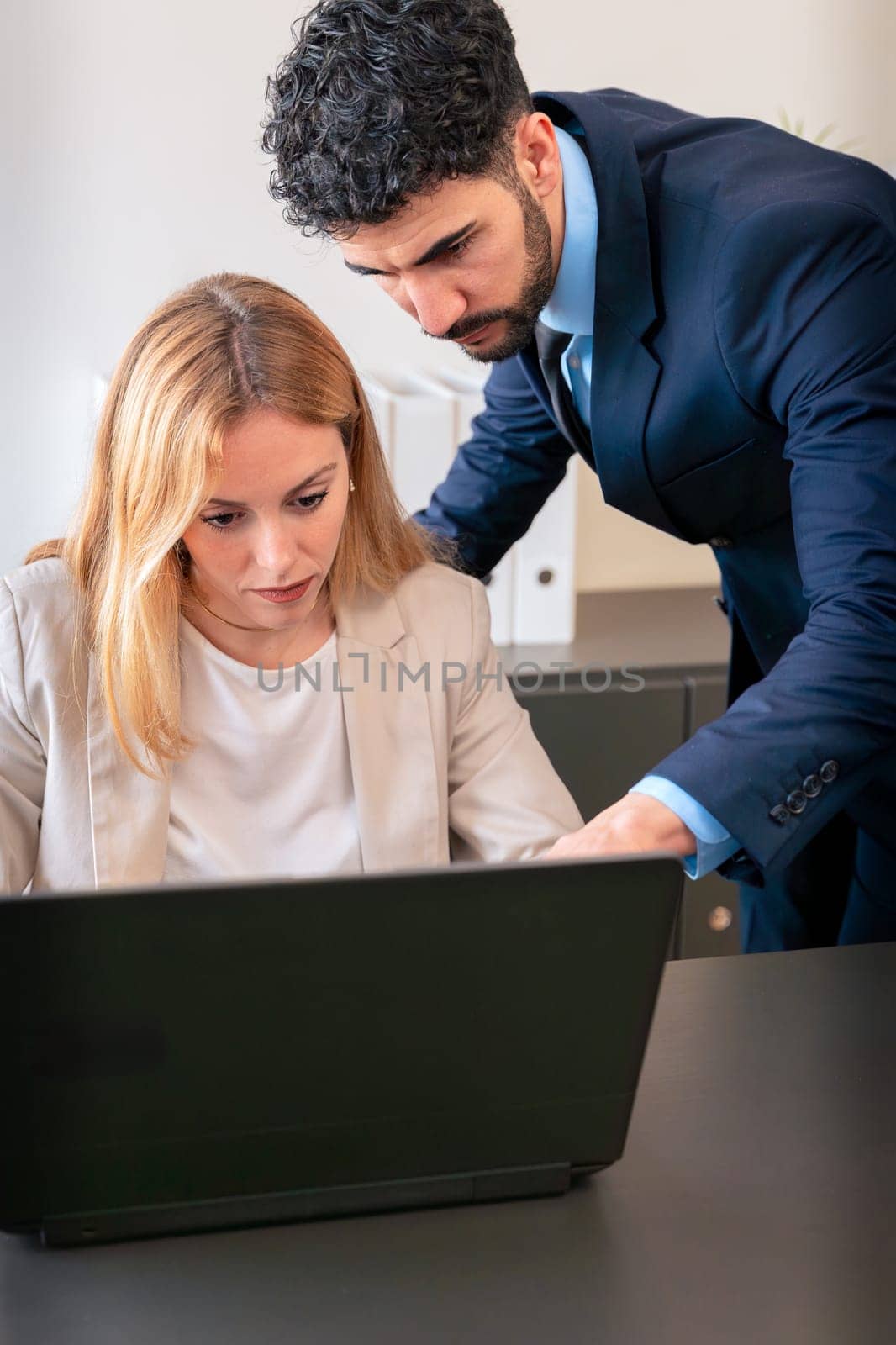 Professional man and woman working together on a laptop in a modern office. The woman points at the screen, explaining details while the man listens attentively.
