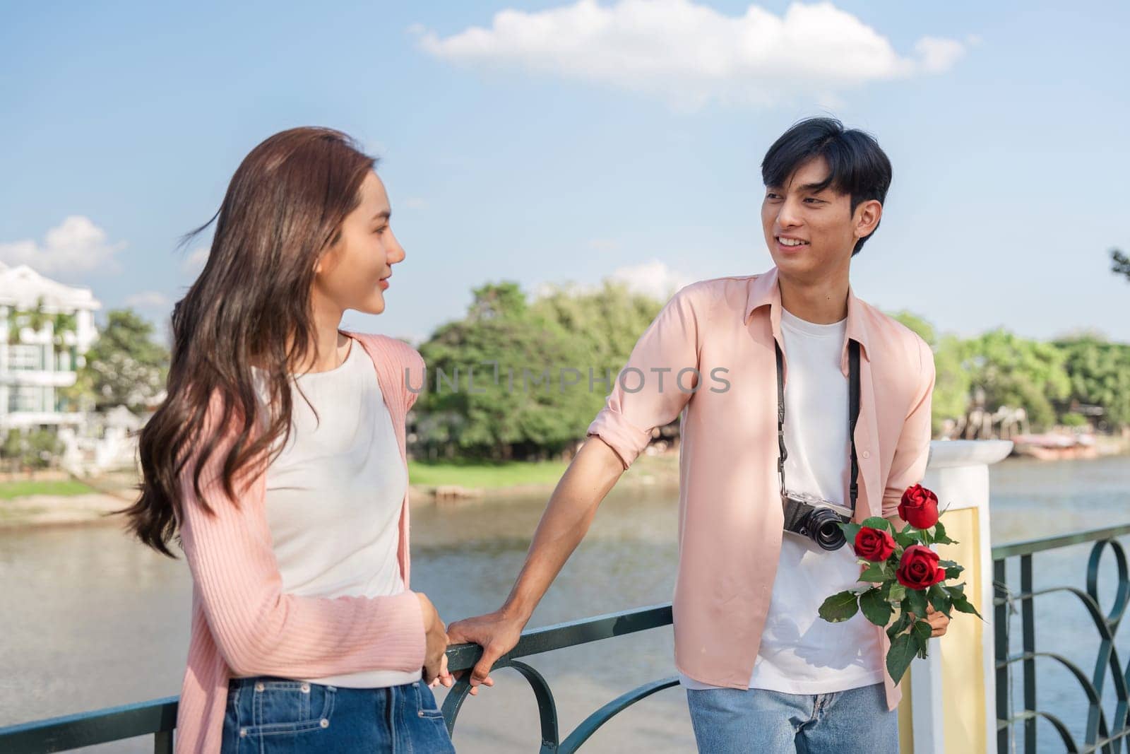 A couple shares a tender moment by the riverside embracing love with roses and a camera perfect for Valentine's Day.