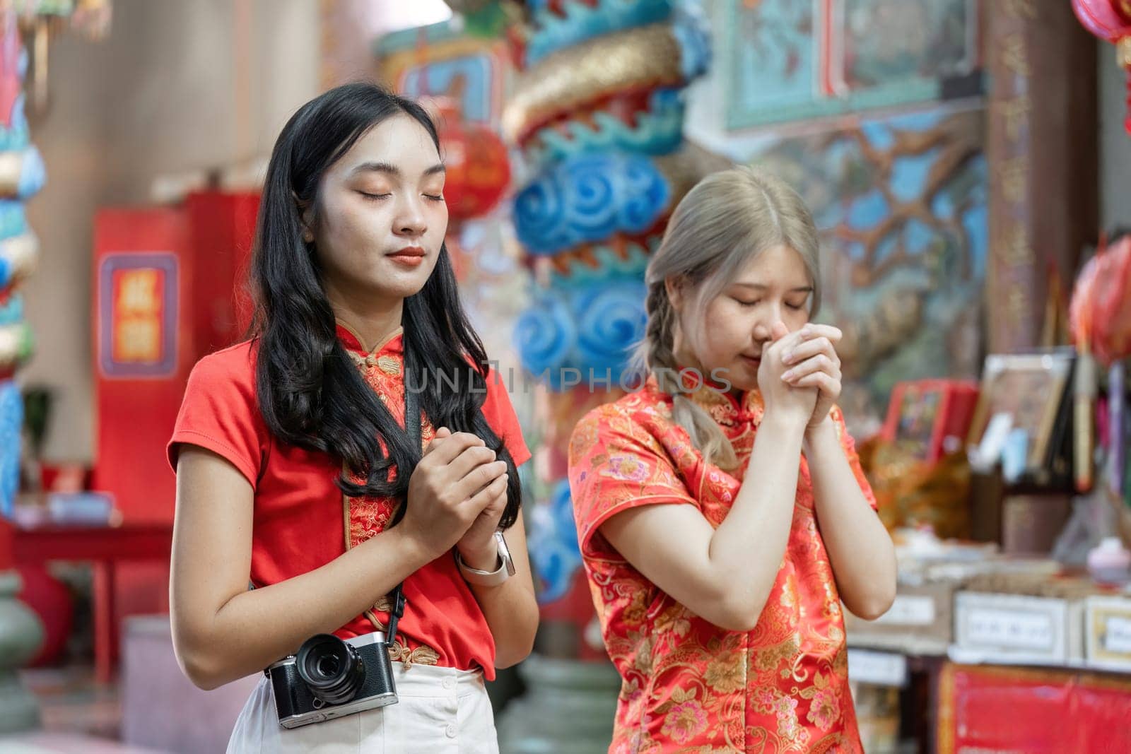 Two women in traditional attire engage in worship at a shrine during Chinese New Year reflecting cultural reverence and celebration.