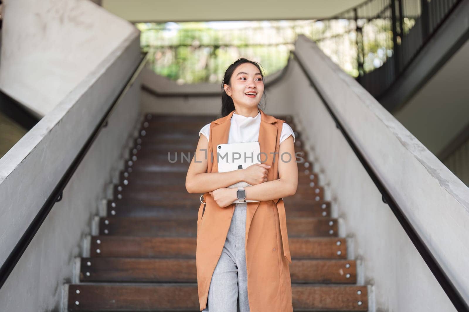 Confident businesswoman ascending stairs with a tablet, symbolizing success and leadership in a modern office environment.
