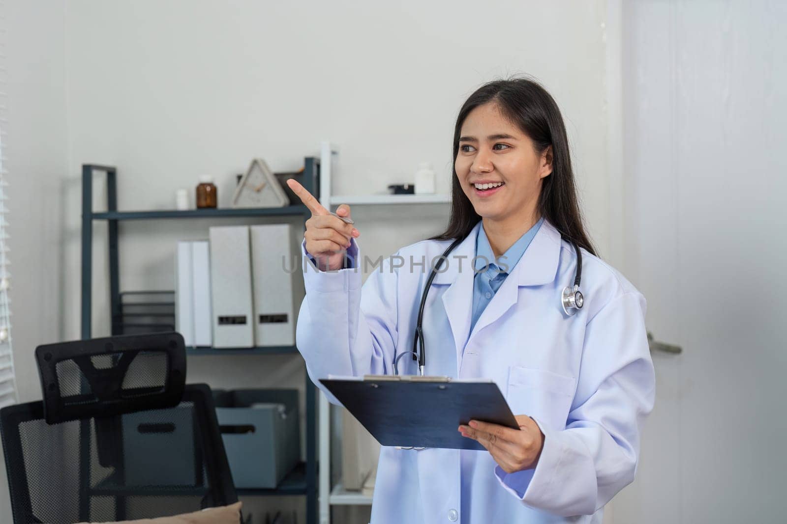 Confident female doctor smiling in a modern office, holding a clipboard and stethoscope, representing professionalism in healthcare.