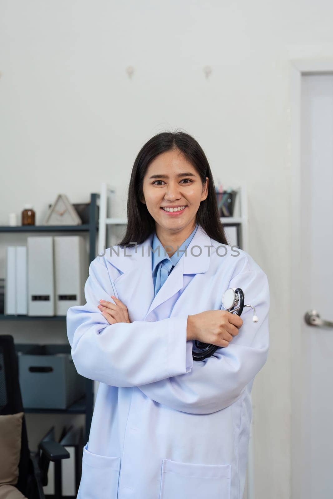 Portrait of a confident female doctor in a white coat, smiling and holding a stethoscope in a modern medical office.