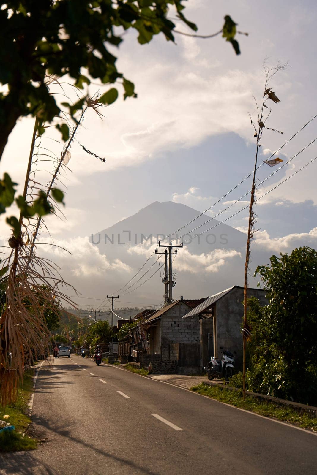 View of the volcano from the road decorated for the holiday in the village. Bamboo decorations along the road. A panorama of Mount Agung covered in clouds before sunset