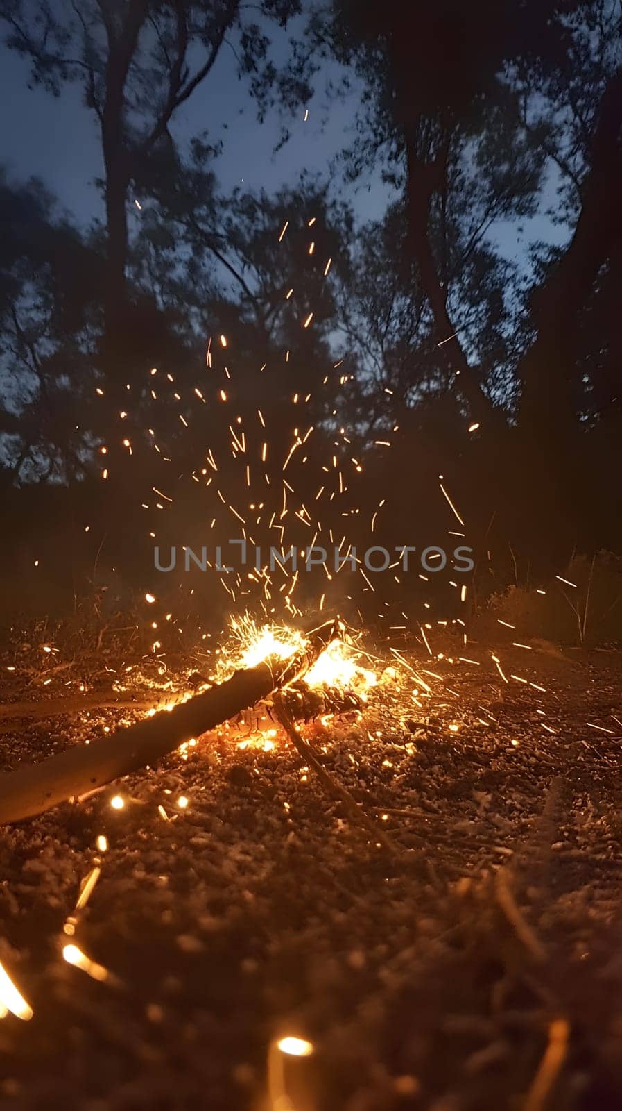A close-up of a glowing campfire with sparks flying in the night.