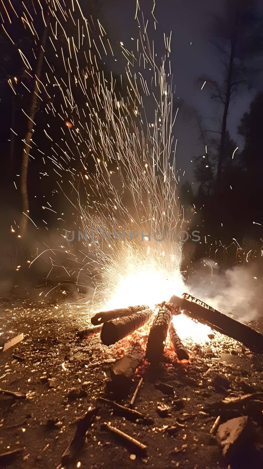 A vibrant campfire sparks at night, illuminating the surrounding area.