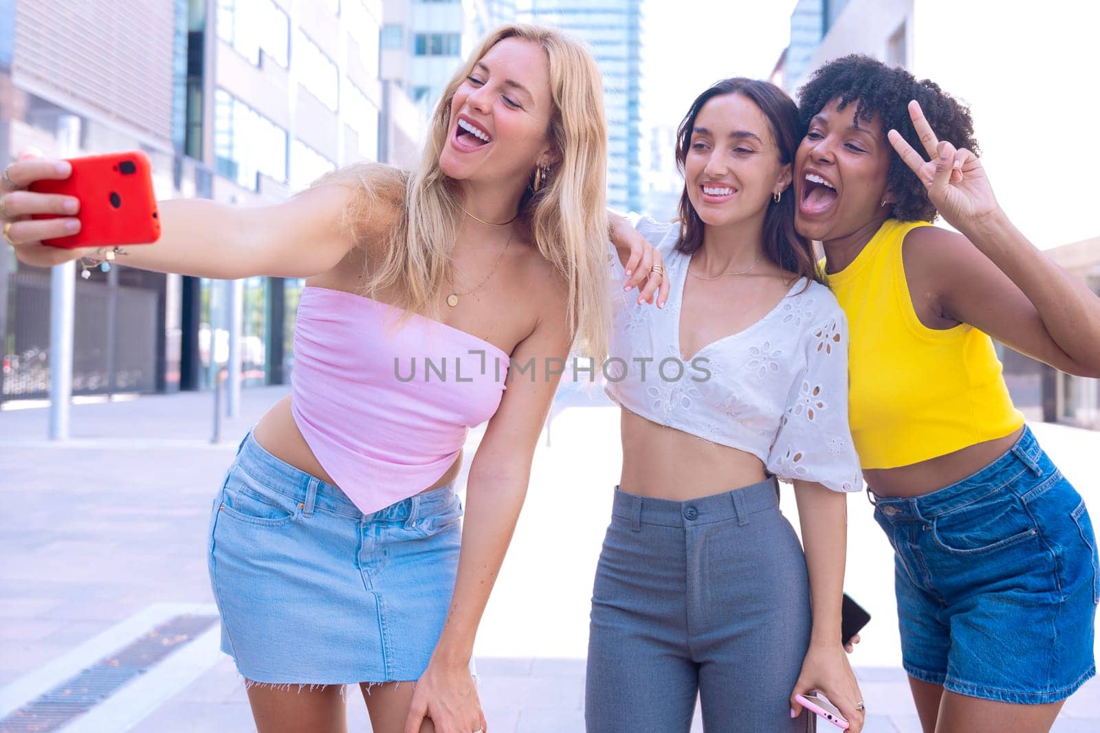 Three young women outdoors, smiling, and taking a playful selfie together. Perfect for concepts like friendship, happiness, social media, and outdoor lifestyle.