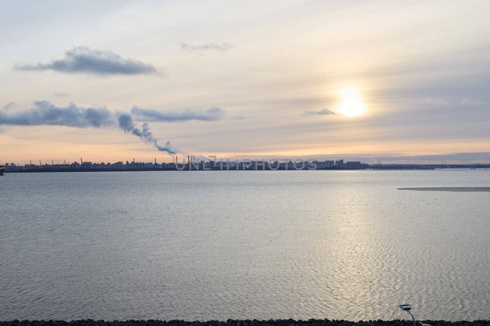 A tranquil sunset softly reflects on serene waters, beautifully framed by a lovely cityscape and gentle clouds