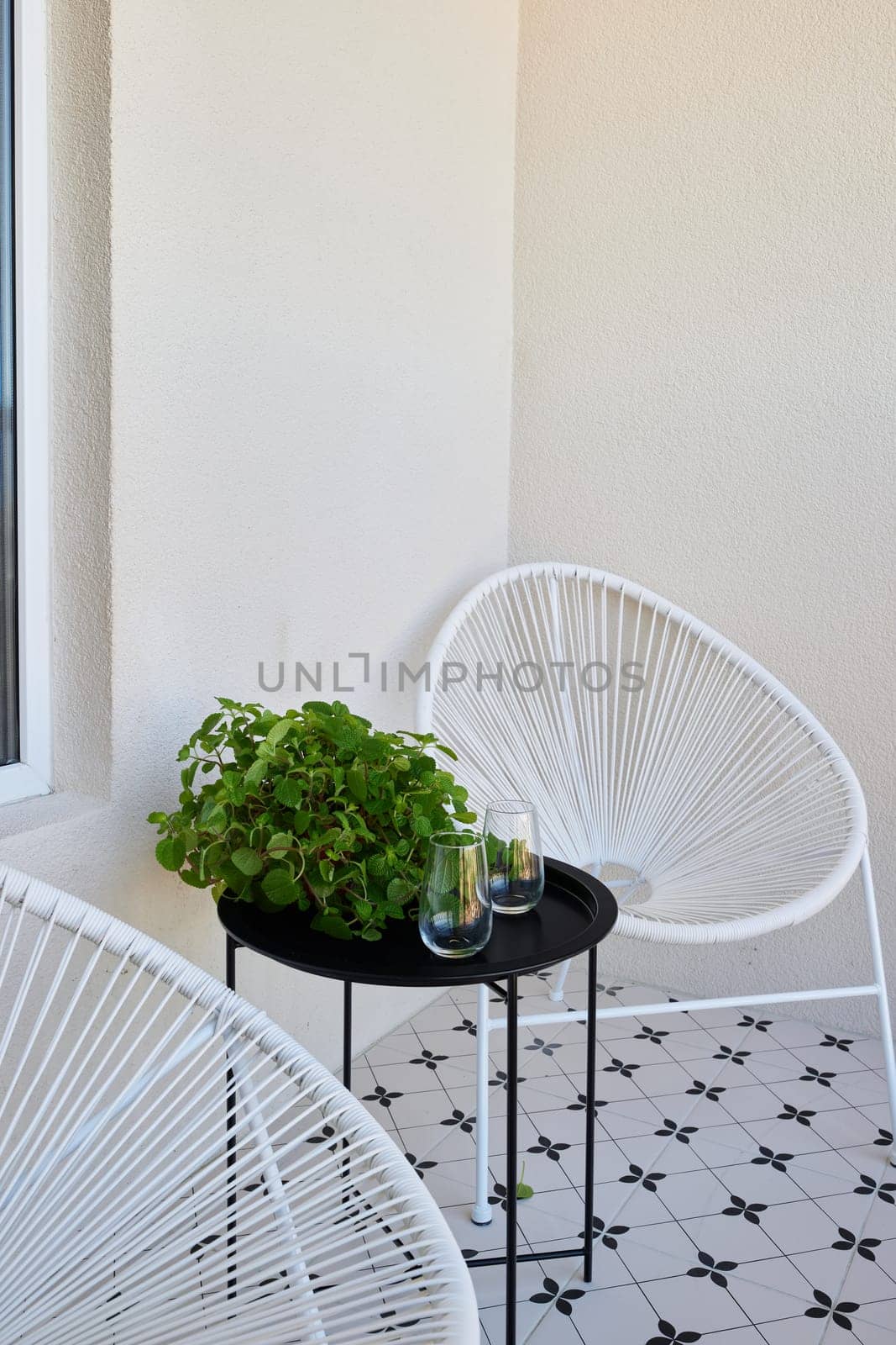 A chic balcony outfitted with elegant chairs, a small table, and vibrant lush greenery offers the perfect escape
