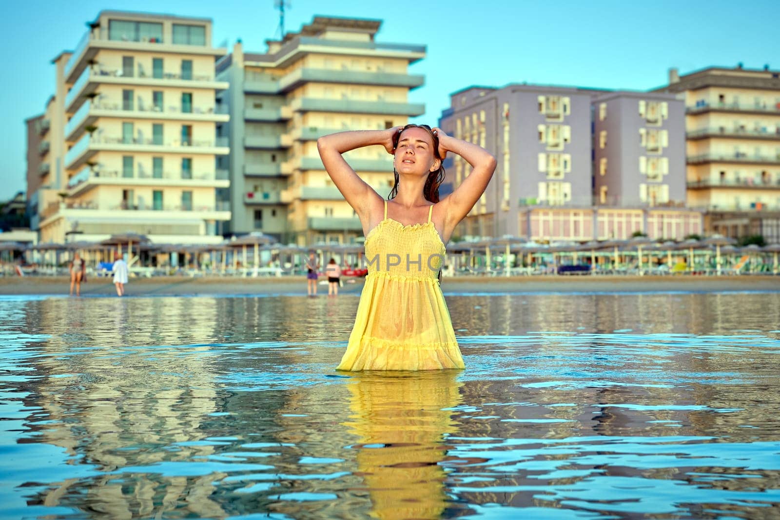 Young woman standing in the sea in front of hotels, enjoying summer holidays