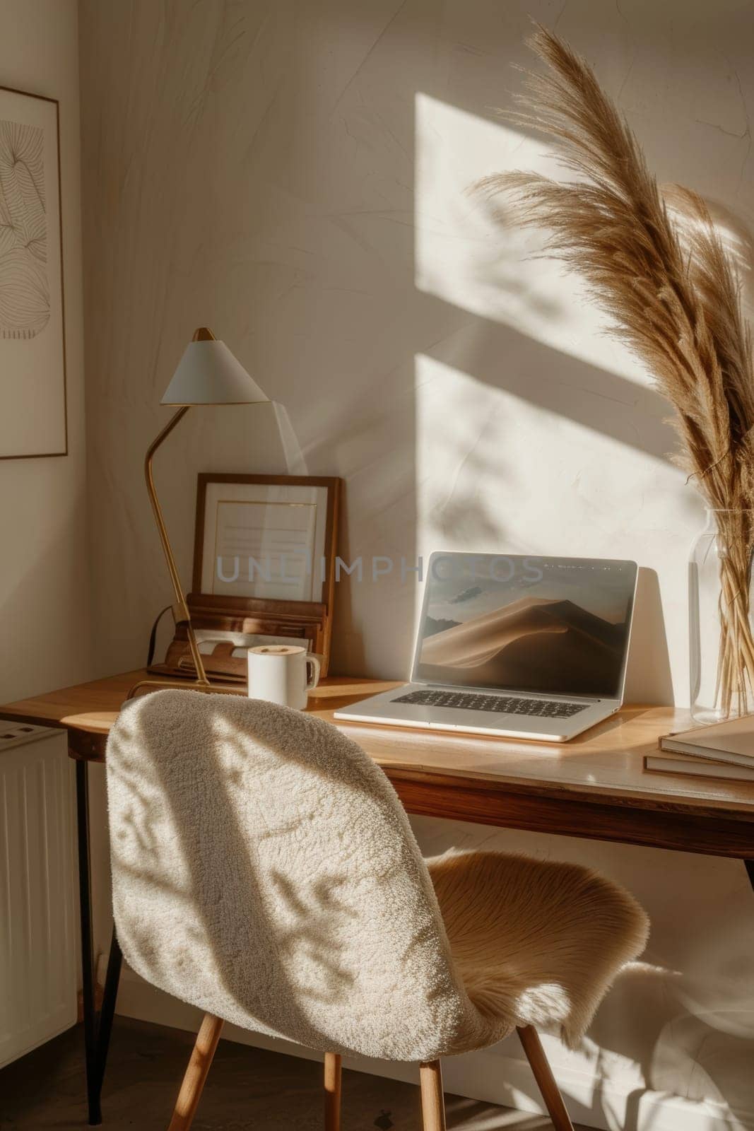Cozy home office scene with a mocha mousse desk chair, a sleek lamp, and a laptop on a wooden desk. styled with a clear vase holding pampas grass, creating an inviting and stylish work area perfect for productivity and inspiration.