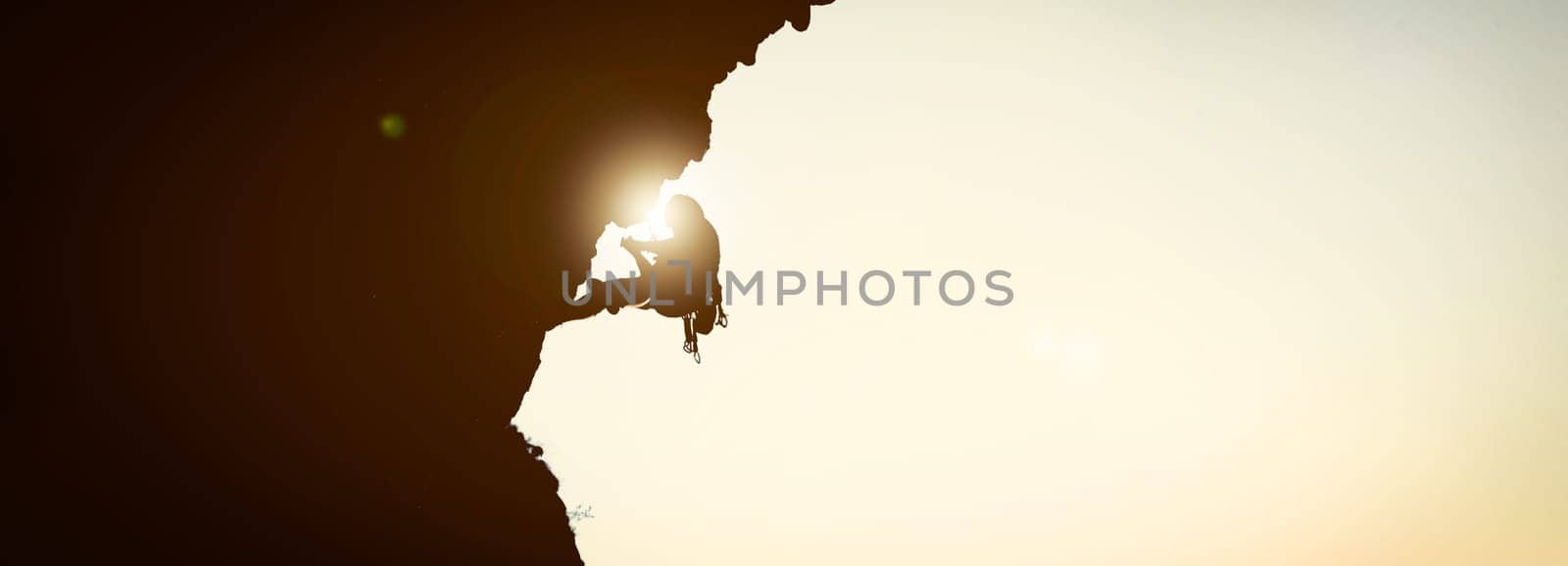 The black silhouette of a person climbs up the mountain against the background of the sky, leading an active lifestyle and involved in extreme sports, mountaineering and rock climbing.