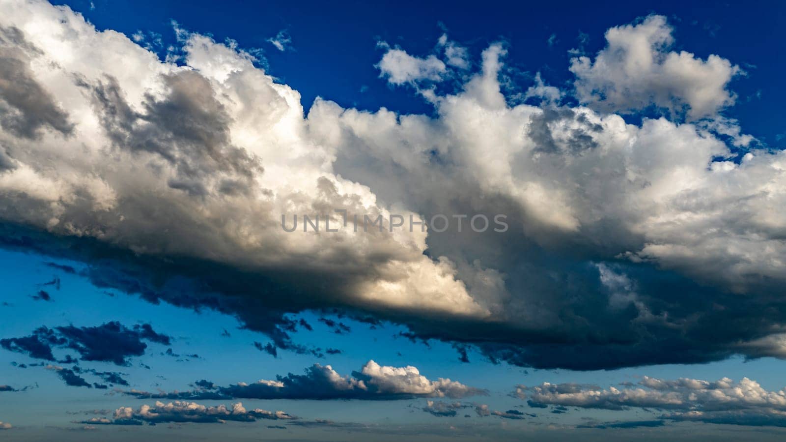 Vast clouds gather and disperse in a vibrant blue sky, creating striking patterns and shapes in the late afternoon light, showcasing nature's beauty and ever-changing weather.
