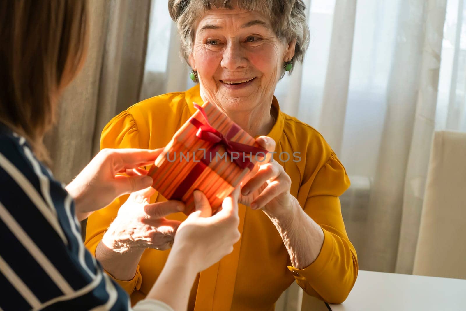 A young girl congratulates an elderly woman, her mother or grandmother, daughter holds in her hands a small cute beautifully wrapped gift for her grandparent, gives a surprise with love and care.