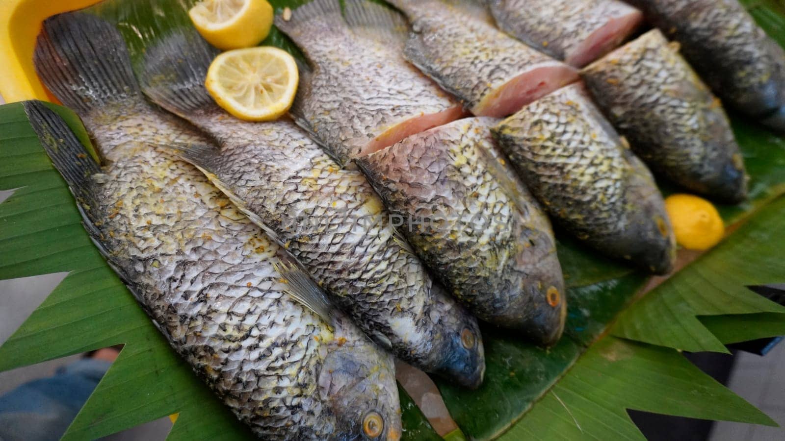 Whole range Guorami fish some kind of tilapia fish prepared for cooking or sale in supermarket are neatly arranged on banana leaves and garnished with lemons, this setup highlights seafood, tropical cuisine, and fresh ingredients for meals.