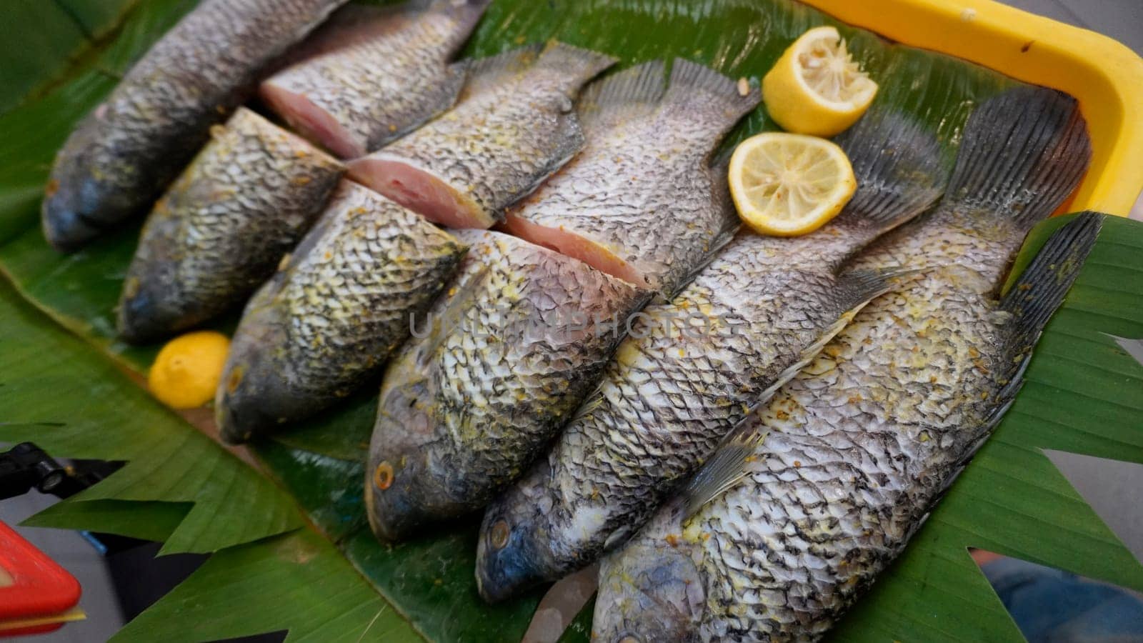 Whole range Guorami fish some kind of tilapia fish prepared for cooking or sale in supermarket are neatly arranged on banana leaves and garnished with lemons, this setup highlights seafood, tropical cuisine, and fresh ingredients for meals.