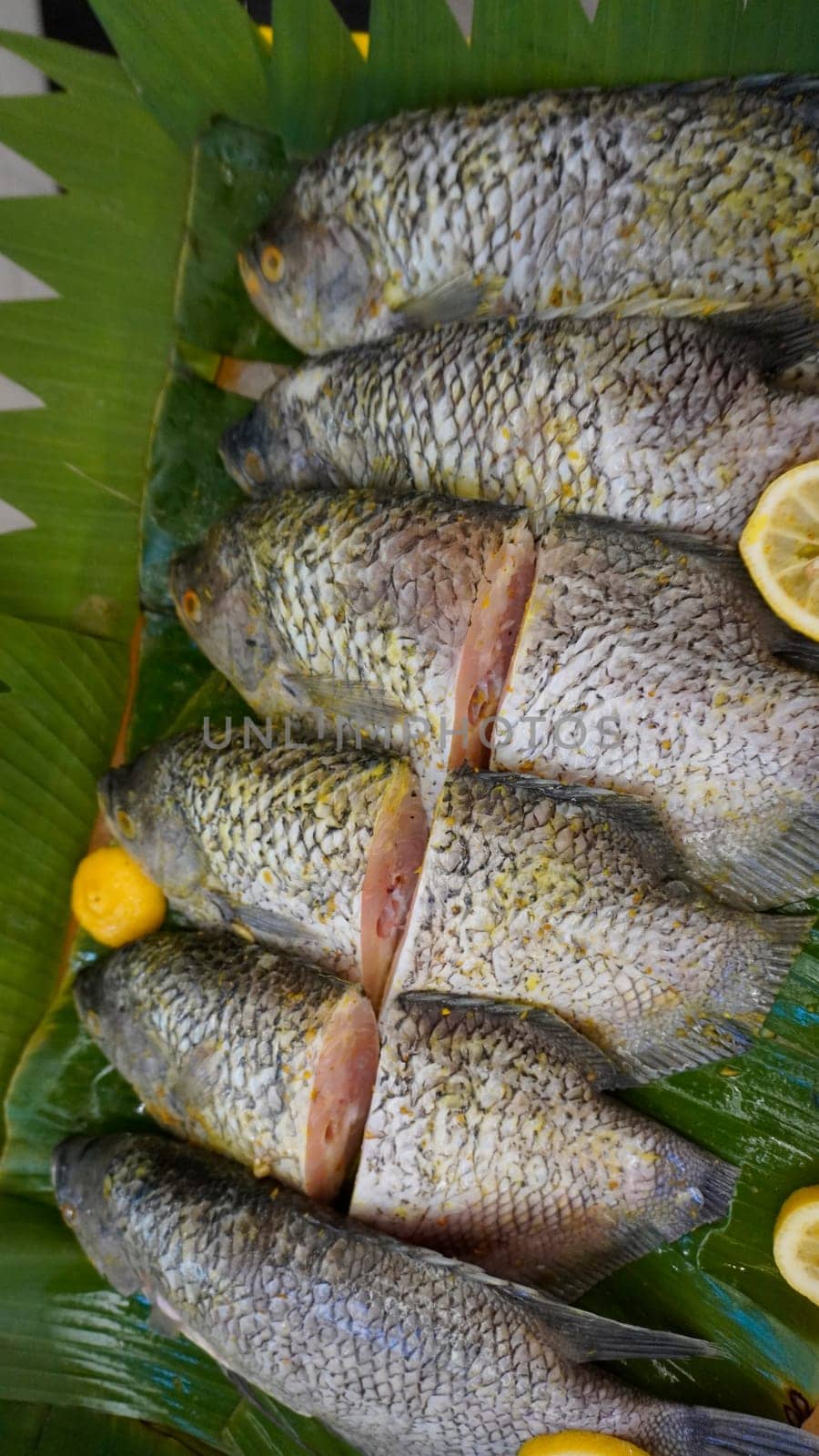 Whole range Guorami fish some kind of tilapia fish prepared for cooking or sale in supermarket are neatly arranged on banana leaves and garnished with lemons, this setup highlights seafood, tropical cuisine, and fresh ingredients for meals.