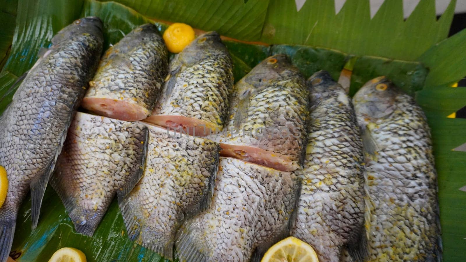 Whole range Guorami fish some kind of tilapia fish prepared for cooking or sale in supermarket are neatly arranged on banana leaves and garnished with lemons, this setup highlights seafood, tropical cuisine, and fresh ingredients for meals.