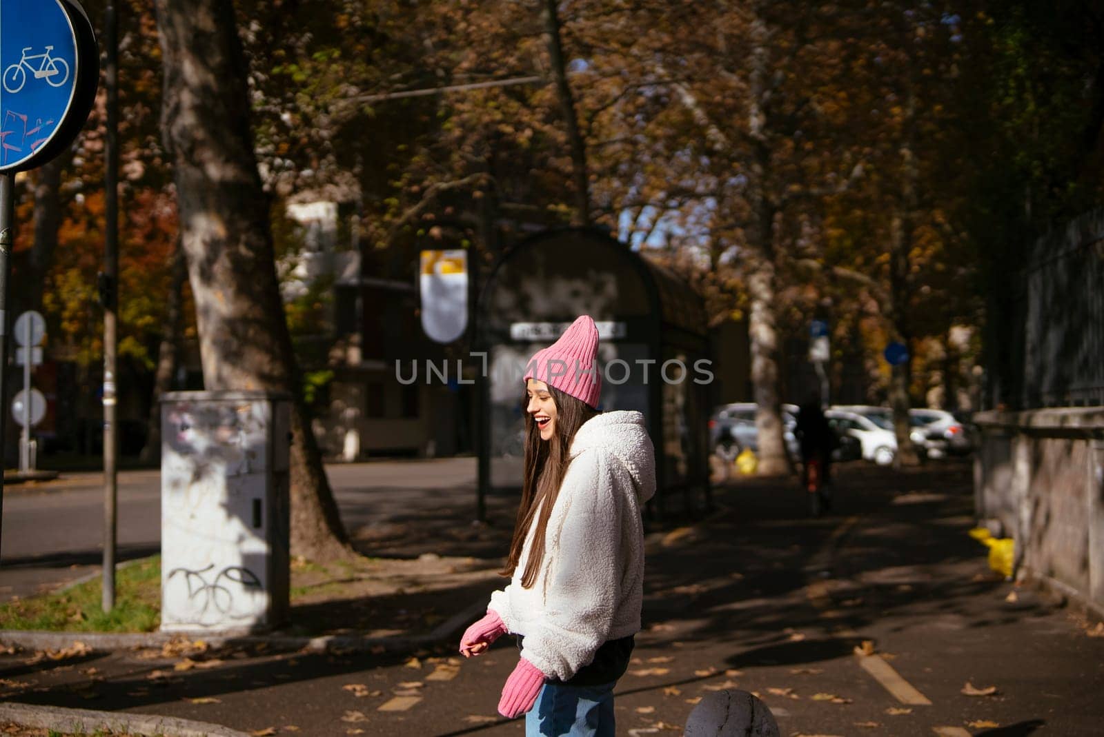 A cheerful woman walks through an autumn park, wrapped in cozy attire, surrounded by colorful foliage.