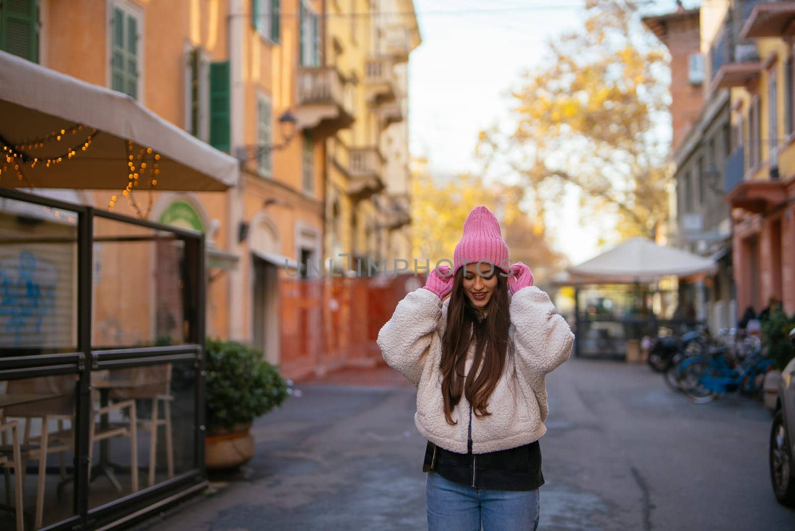 A stylish and fashionable young woman beams with joy while wearing a trendy pink beanie in a picturesque street scene