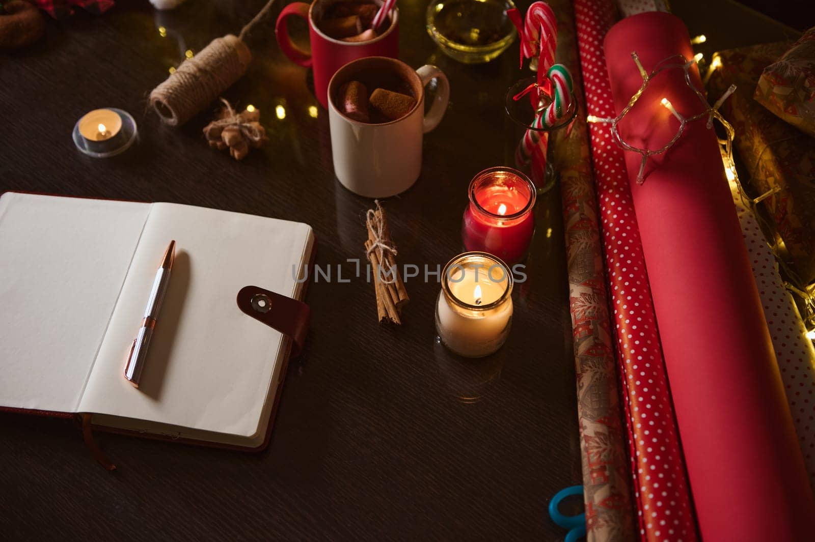 Festive notebook and holiday-themed items such as wrapping paper, candles, and cups on a table.