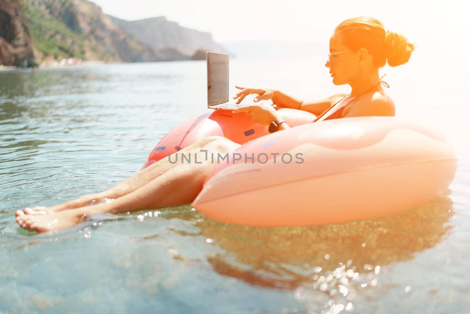 Woman laptop sea. Freelancer woman in sunglases floating on an inflatable big pink donut with a laptop in the sea. People summer vacation rest lifestyle concept by Matiunina