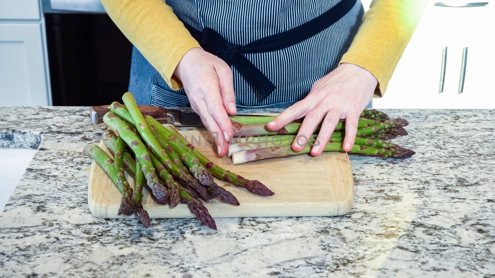 Large organic asparagus stalks are being sliced in a modern white kitchen, in preparation for steaming.