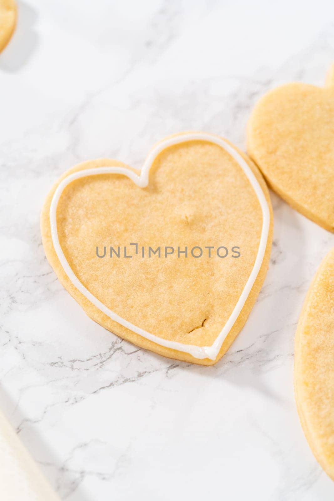 Decorating heart-shaped sugar cookies with pink and white royal icing for Valentine's Day.