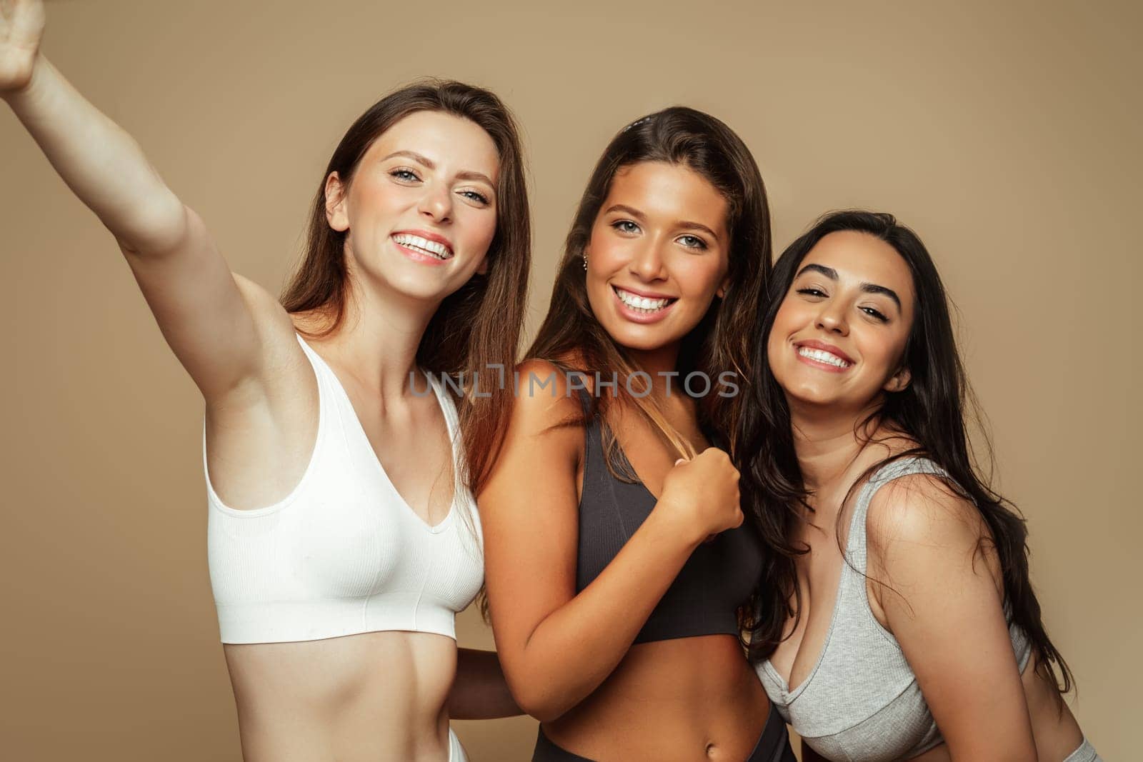 Smiling millennial pretty caucasian, arab, latin women enjoy skin care, make selfie, isolated on beige background. Pride and motivation for self love, spa treatments, wellness, beauty care