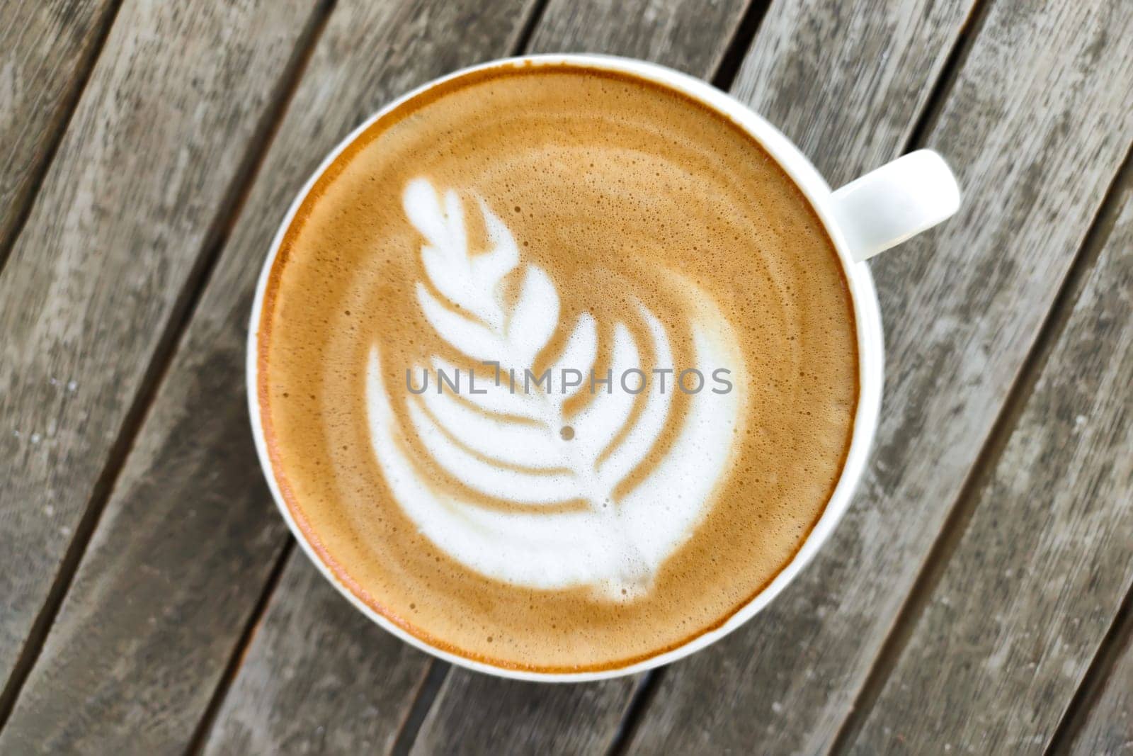 White cup of coffee with pattern on top of foam, against background of wooden table, top view. by Laguna781