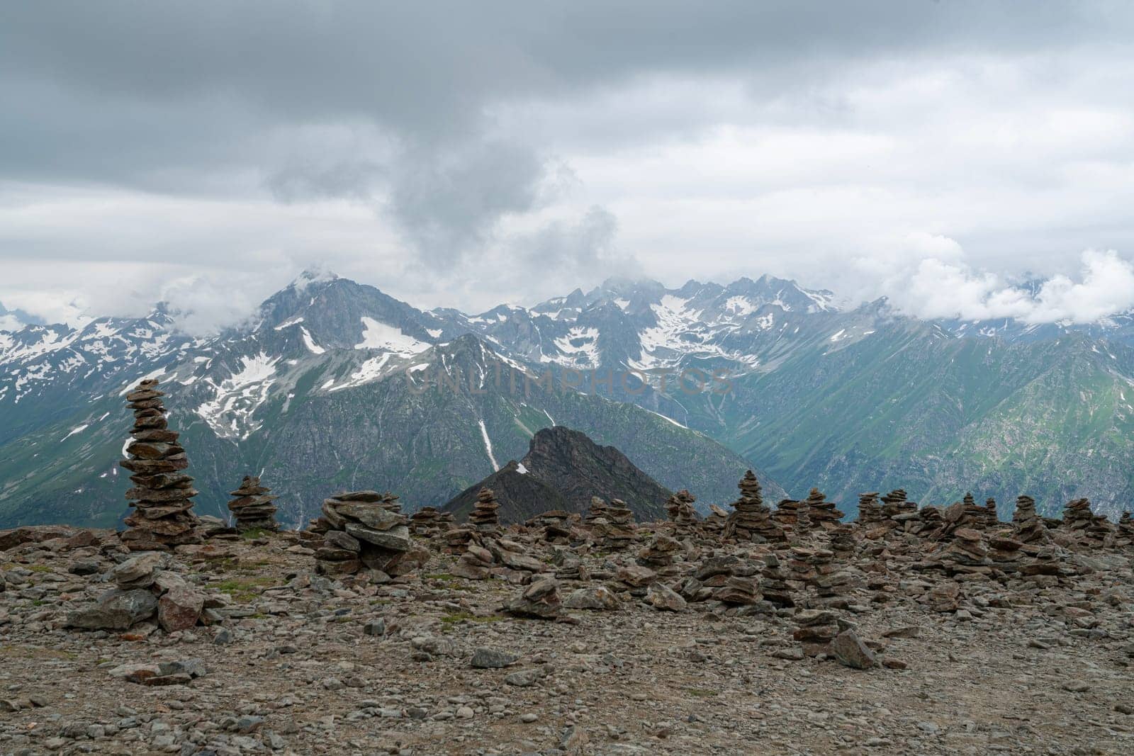 Stacked rock formations create a unique landscape against a backdrop of majestic mountains and cloudy skies. This serene spot showcases nature's beauty and tranquility at elevation.