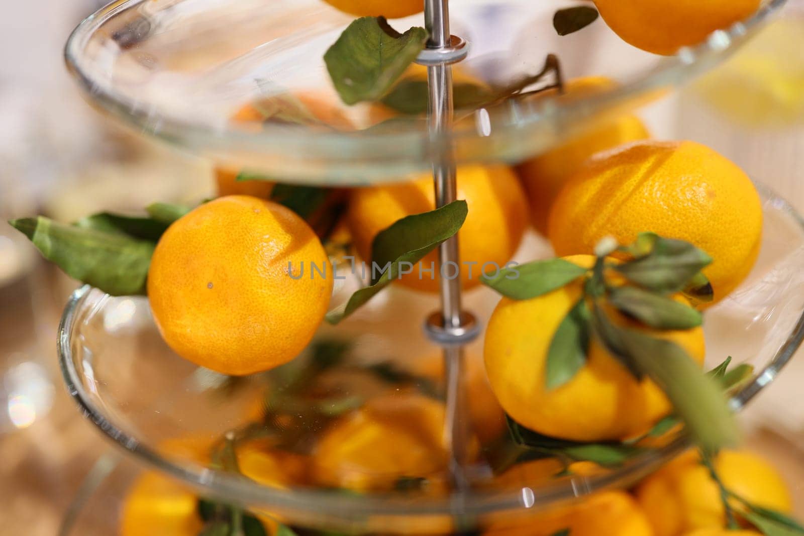 A vibrant display of fresh oranges with green leaves in a glass stand, enhancing any decor with natures touch