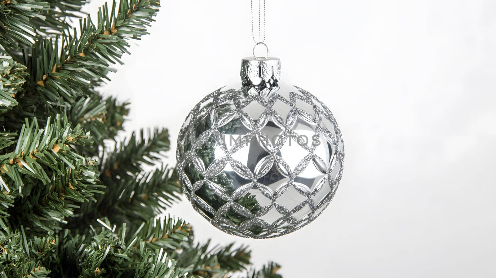 A shiny silver Christmas ornament hanging from a tree branch.