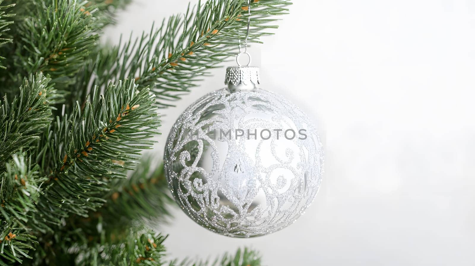 A silver ornament hanging on a Christmas tree branch.