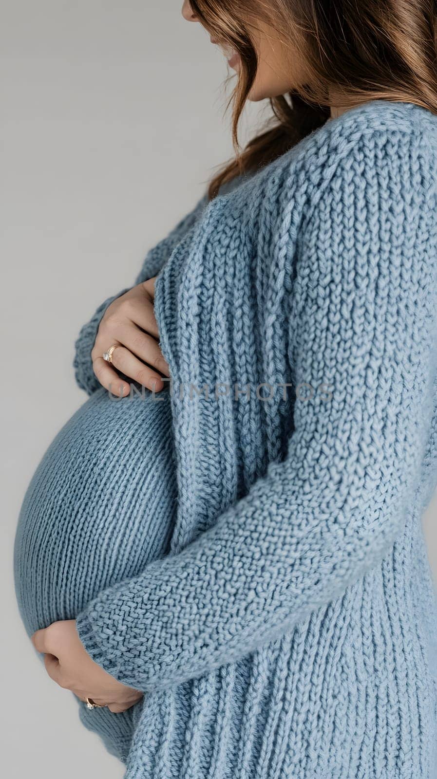 A woman gently cradling her pregnant belly in a cozy sweater.