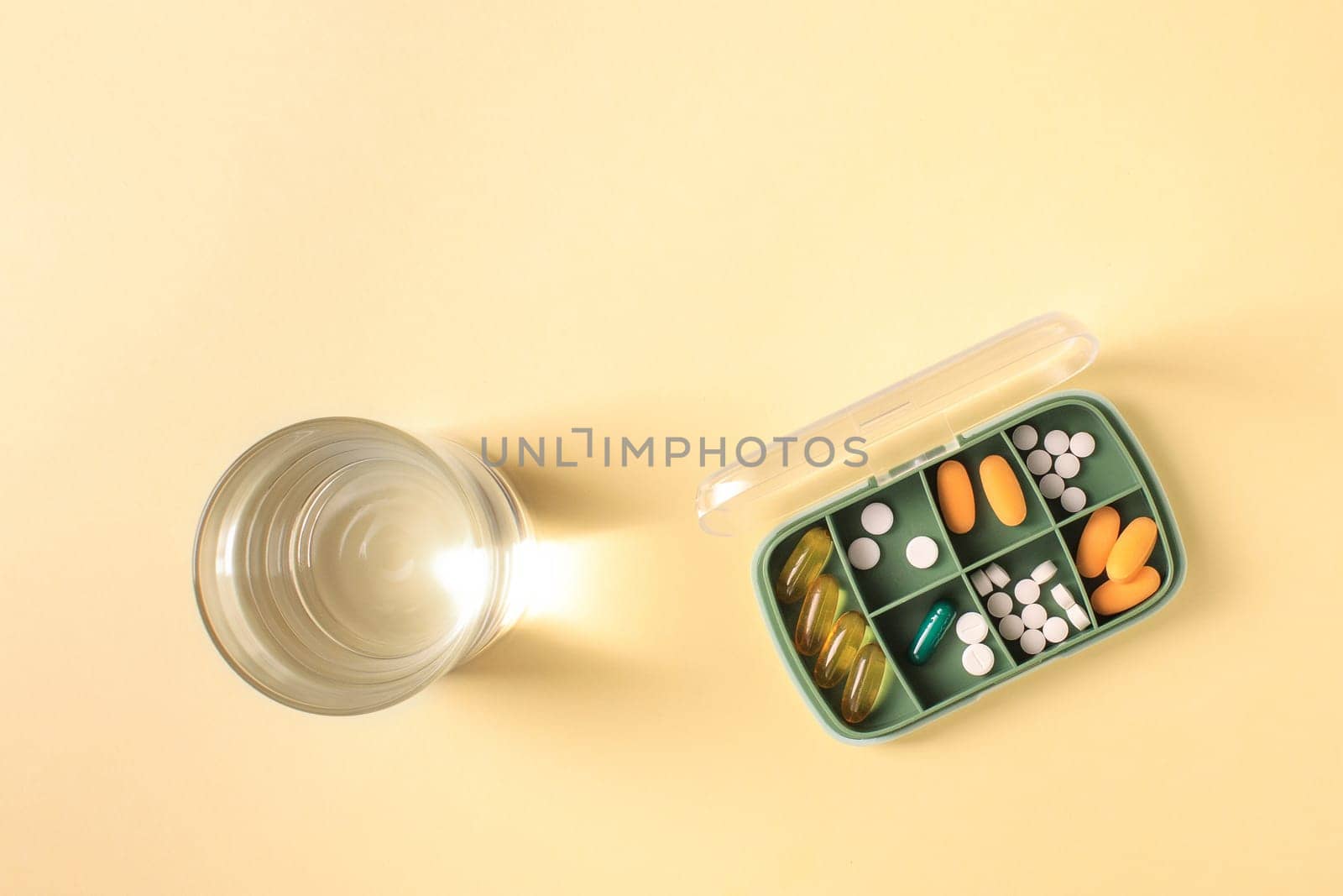Pill box with various pills and vitamins and a glass of water, top view, copy space.