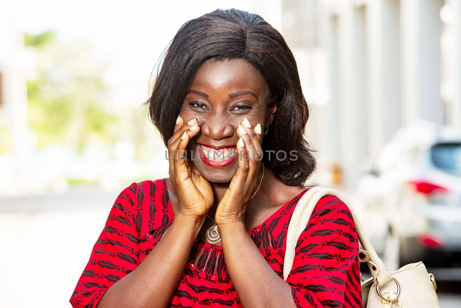 mature african woman standing outdoors looking at camera smiling with handbag.