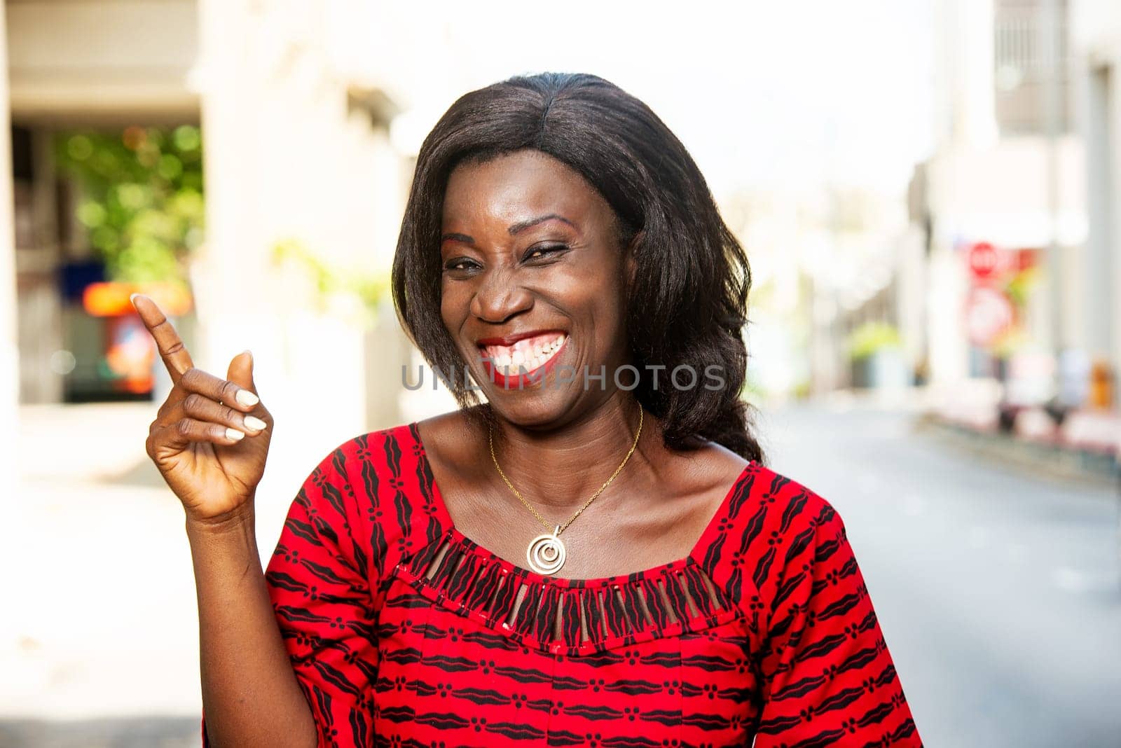 mature african woman standing outdoors looking at camera laughing.
