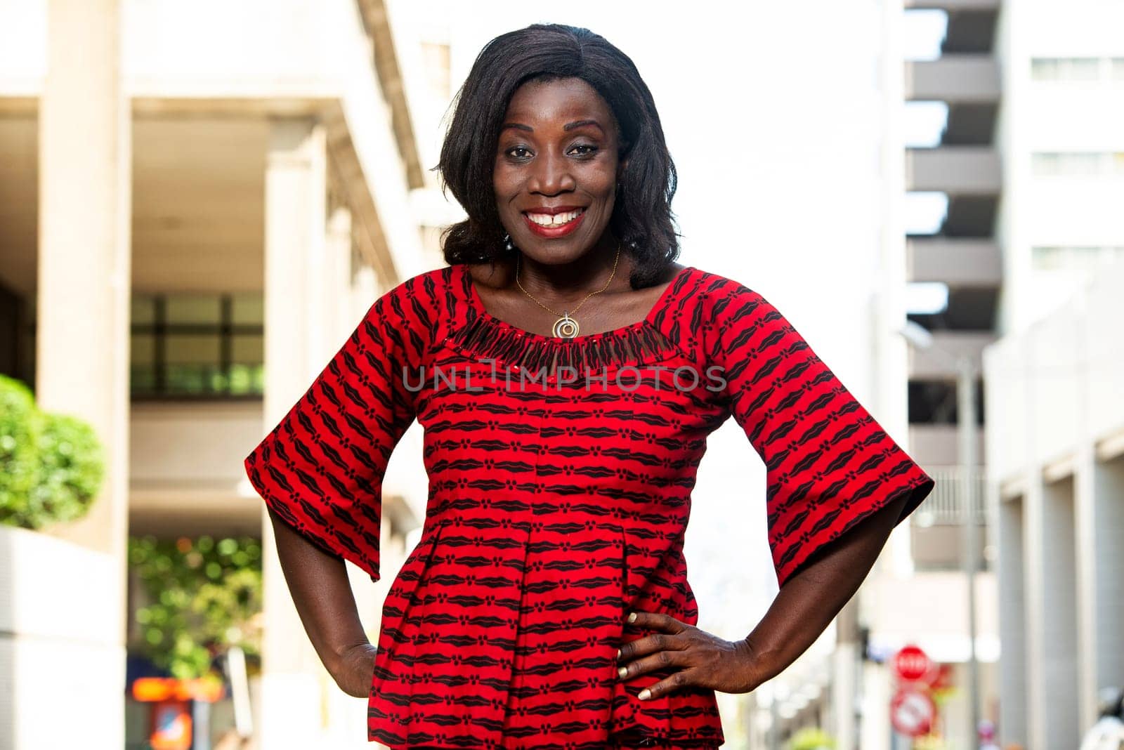 mature african woman standing outdoors looking at camera smiling.