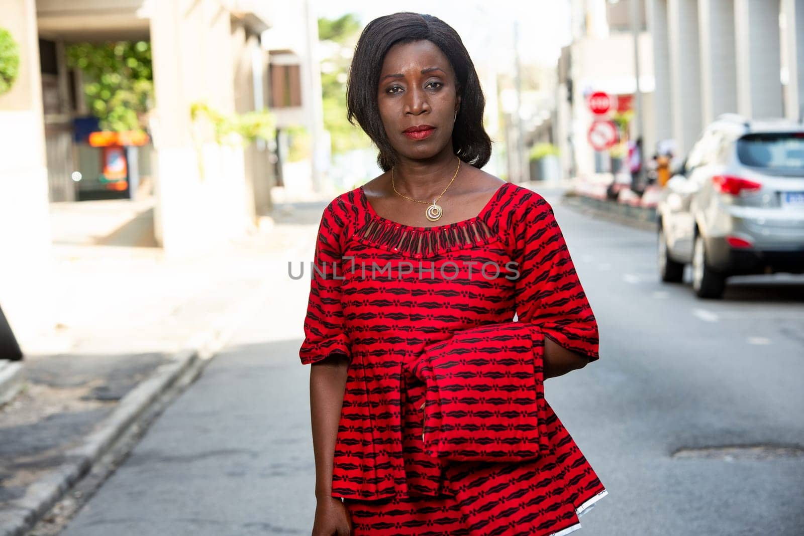 portrait of fashionable african woman posing in red loincloth standing on street in sunny daylight.