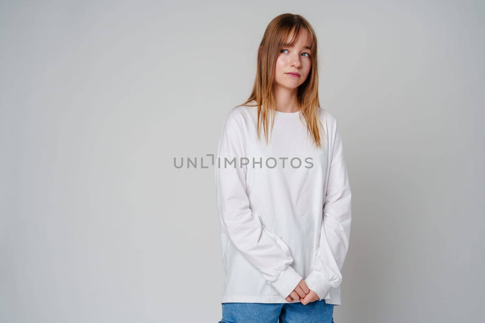 Teen girl stands in casual attire against a plain background, showcasing her thoughtful expression close up