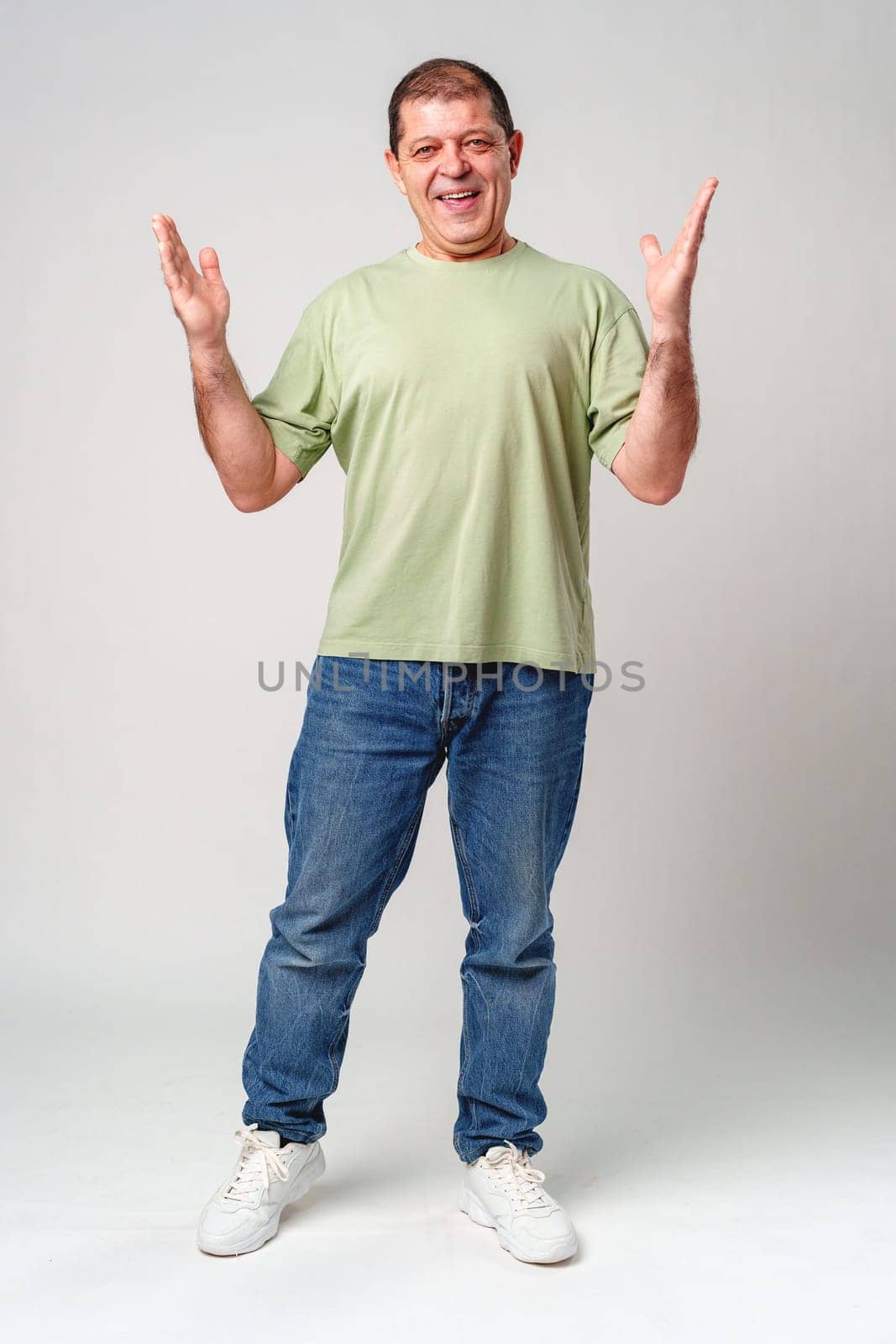 Cheerful man in a green shirt expressing happiness with open hands against a plain background close up