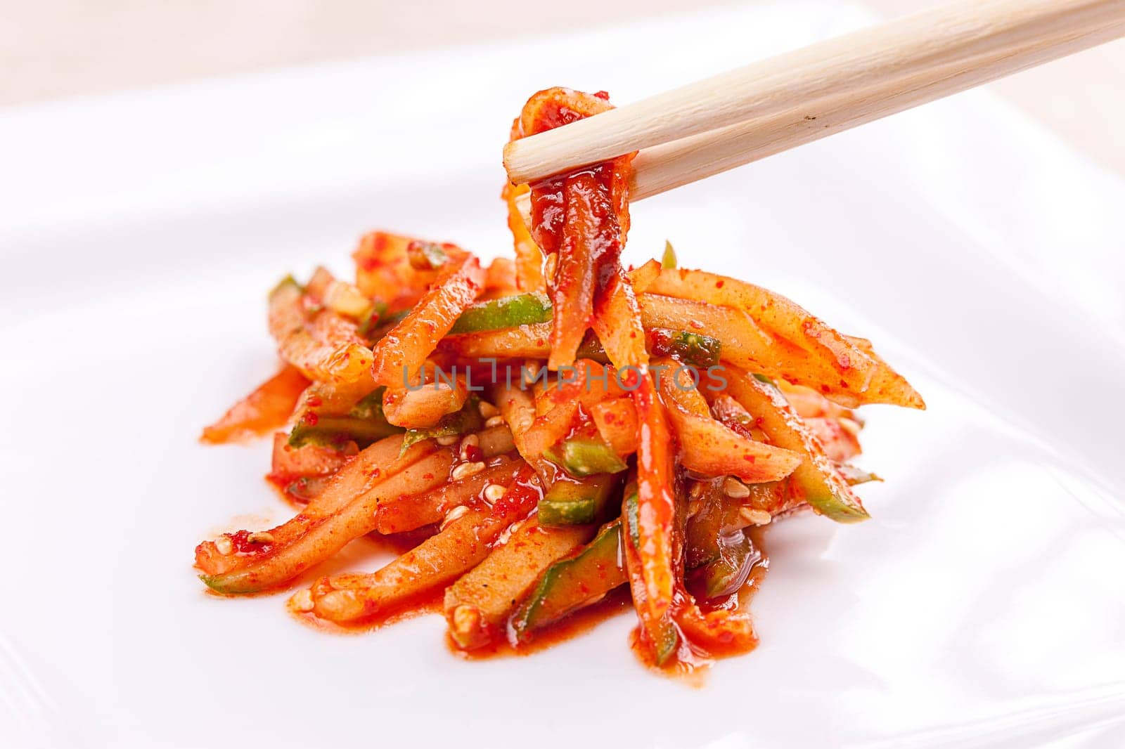 A close up image of sliced cucumbers mixed in red pepper paste and chopsticks.