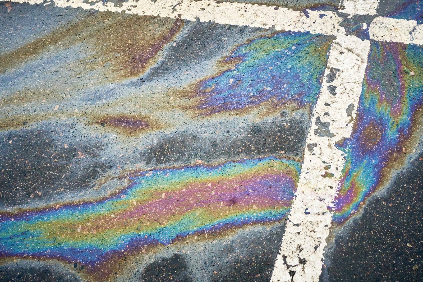 Gasoline or oil spill creating rainbow sheen on asphalt parking lot surface.