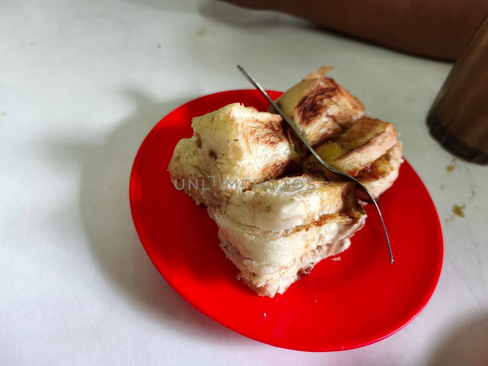 A plate of toasted bread, cut into four pieces, with a fork on top. The bread is lightly browned and looks crispy.