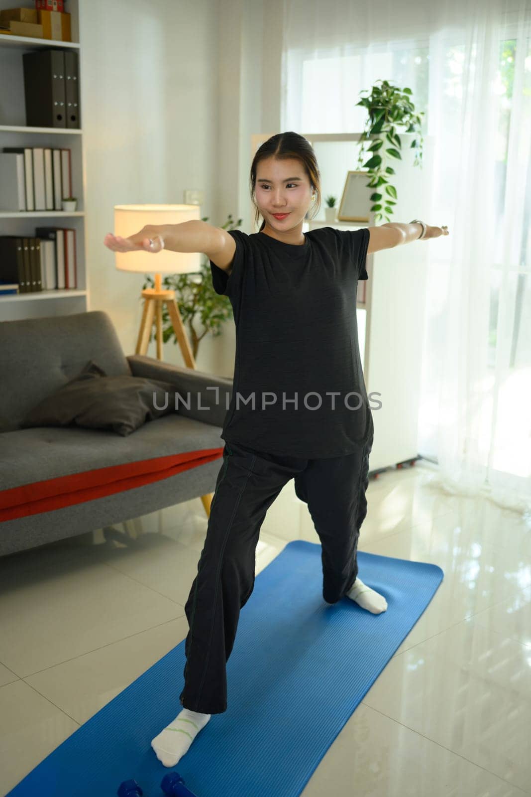 Attractive young woman practicing yoga on mat in living room.