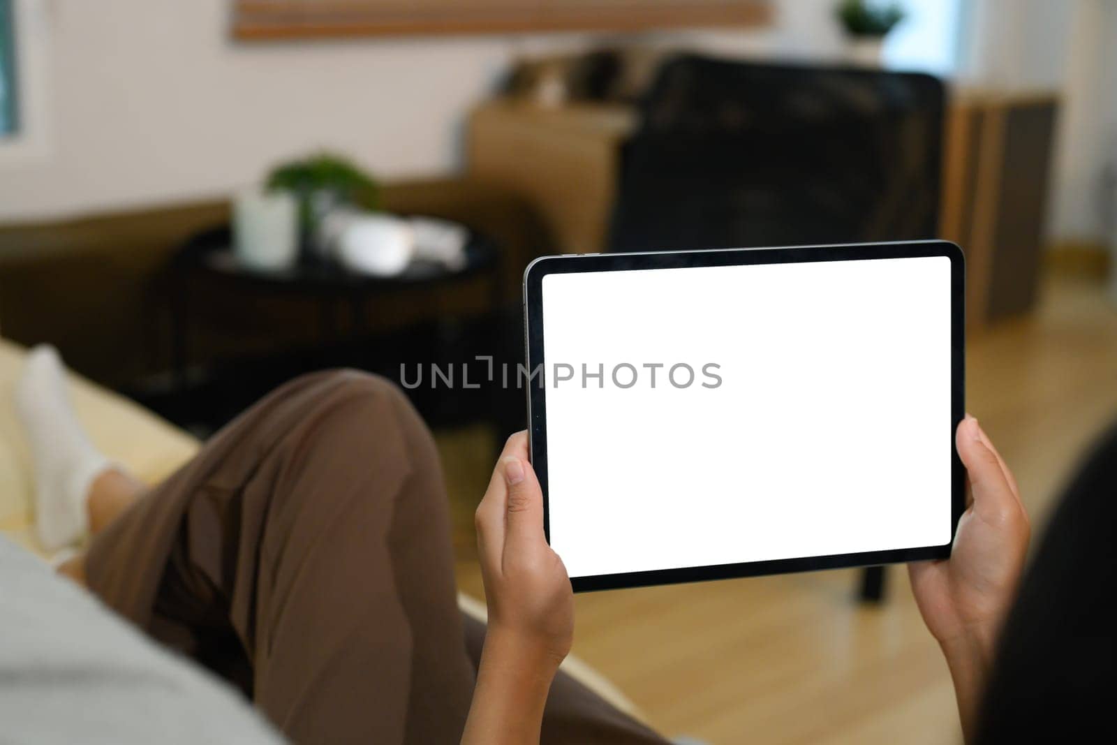 Closeup of hands holding digital tablet with a blank display lying on sofa.