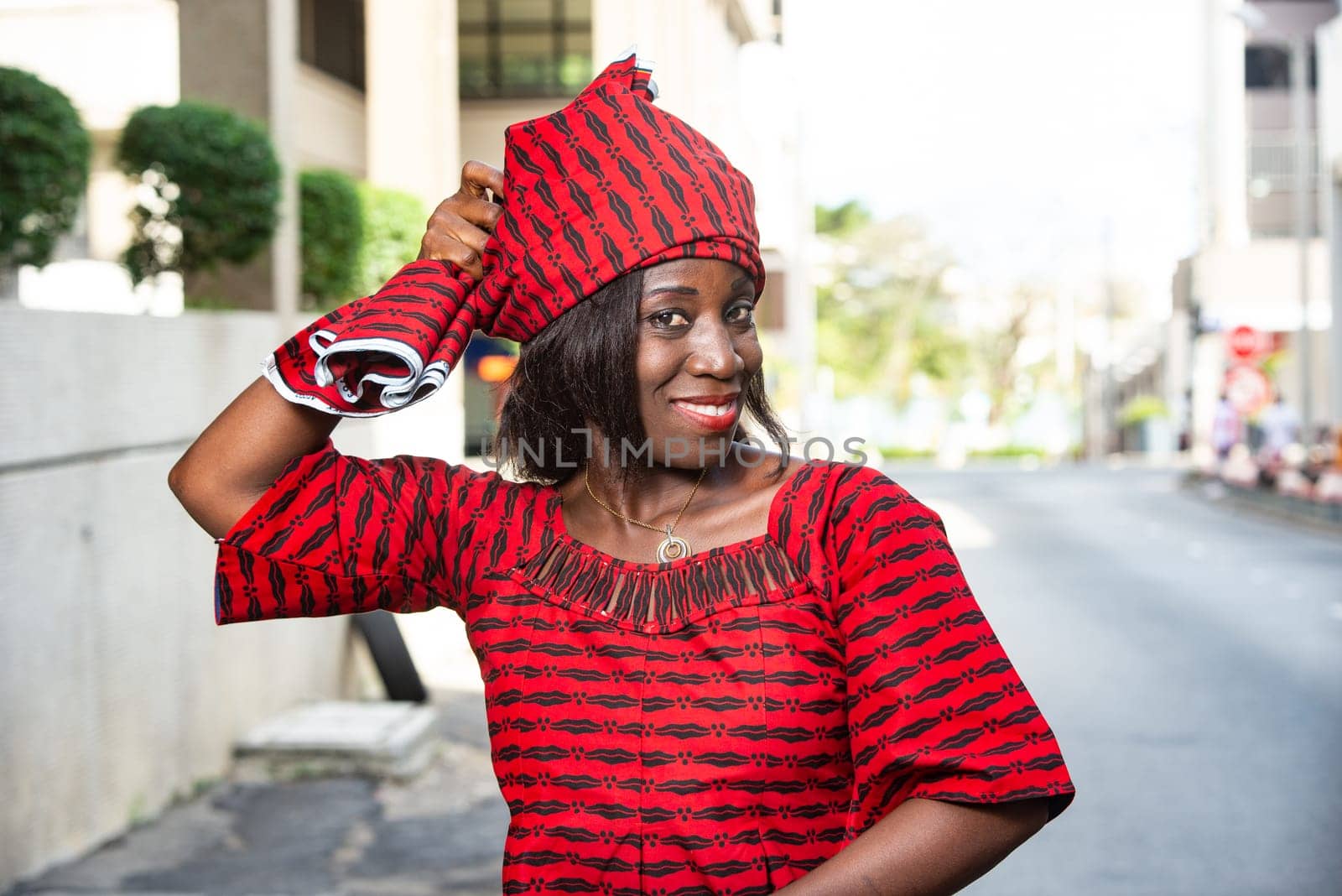 fashionable stylish african woman wearing a red loincloth straps a scarf on her head while smiling in the street in daylight
